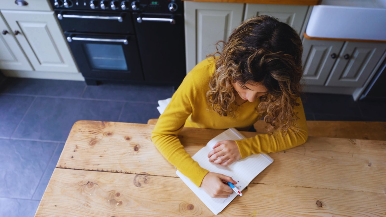 A person with a notebook open on a kitchen table with a few short handwritten lines, soft Sunday evening light.