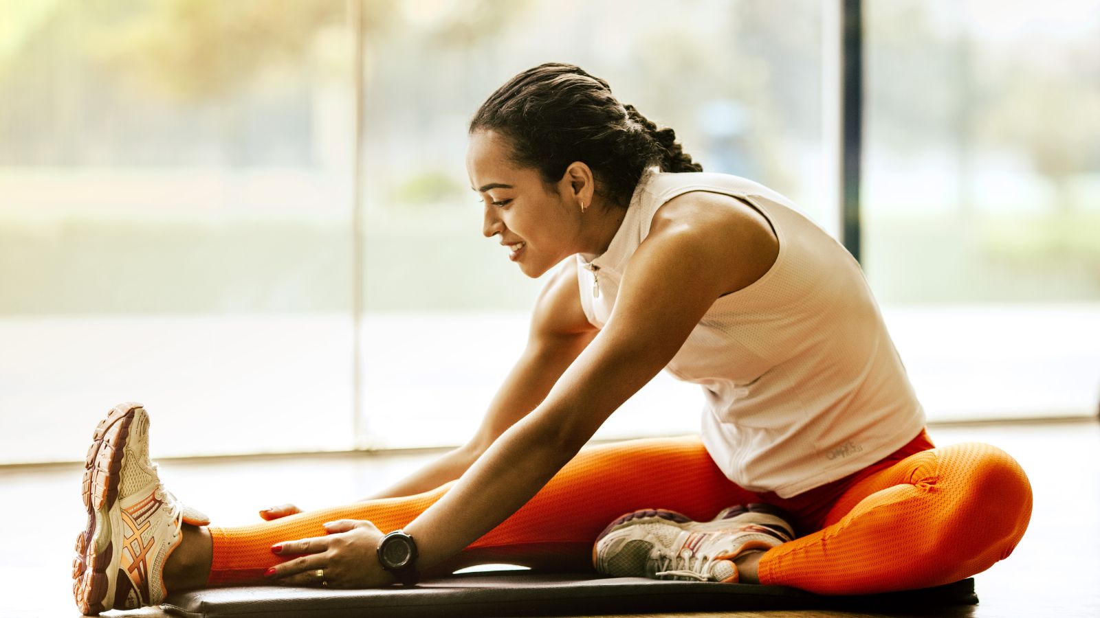 A person sitting, streching with thier arms reaching out towards their foot.