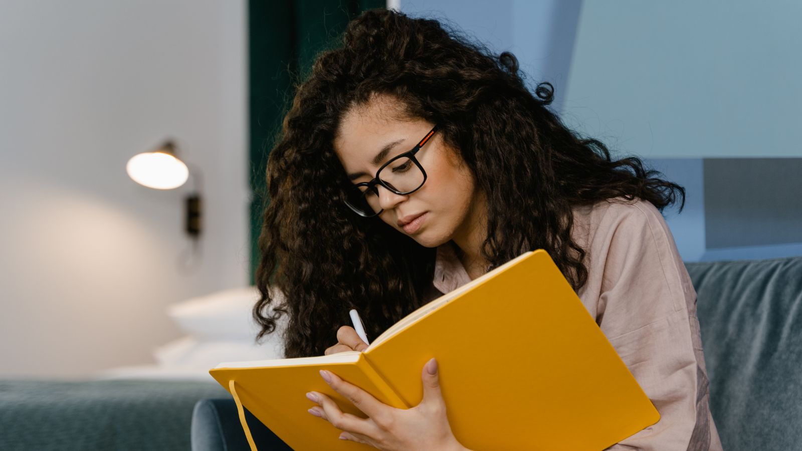 A person writing in a large notebook, looking thoughtful in soft natural light.