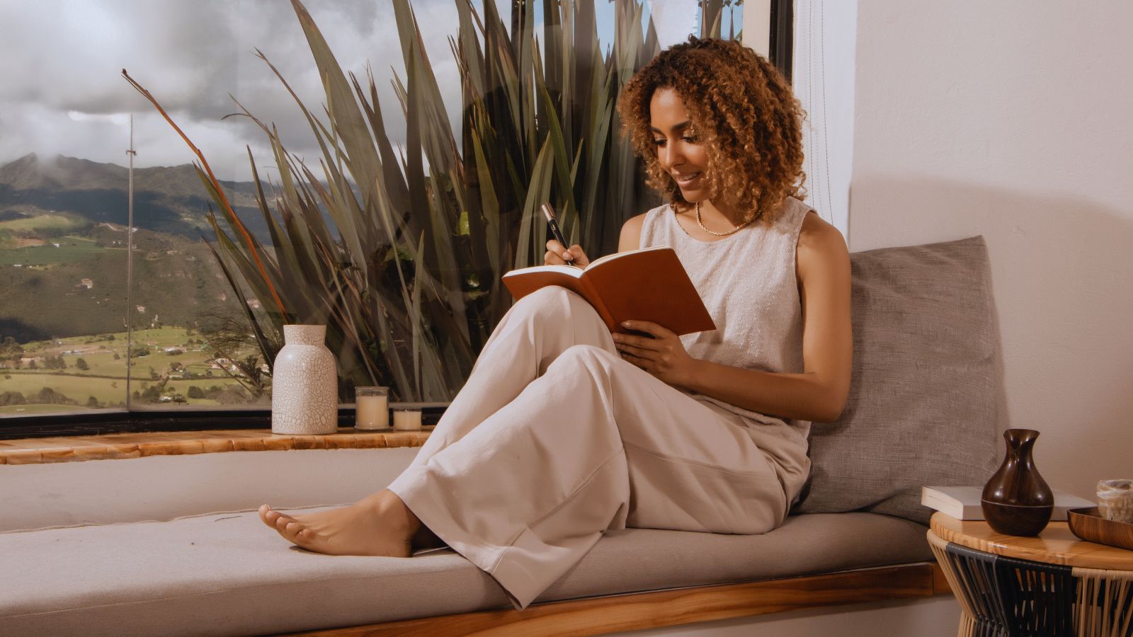 A person sitting at a window with a small notebook open, reviewing past entries in soft afternoon light.
