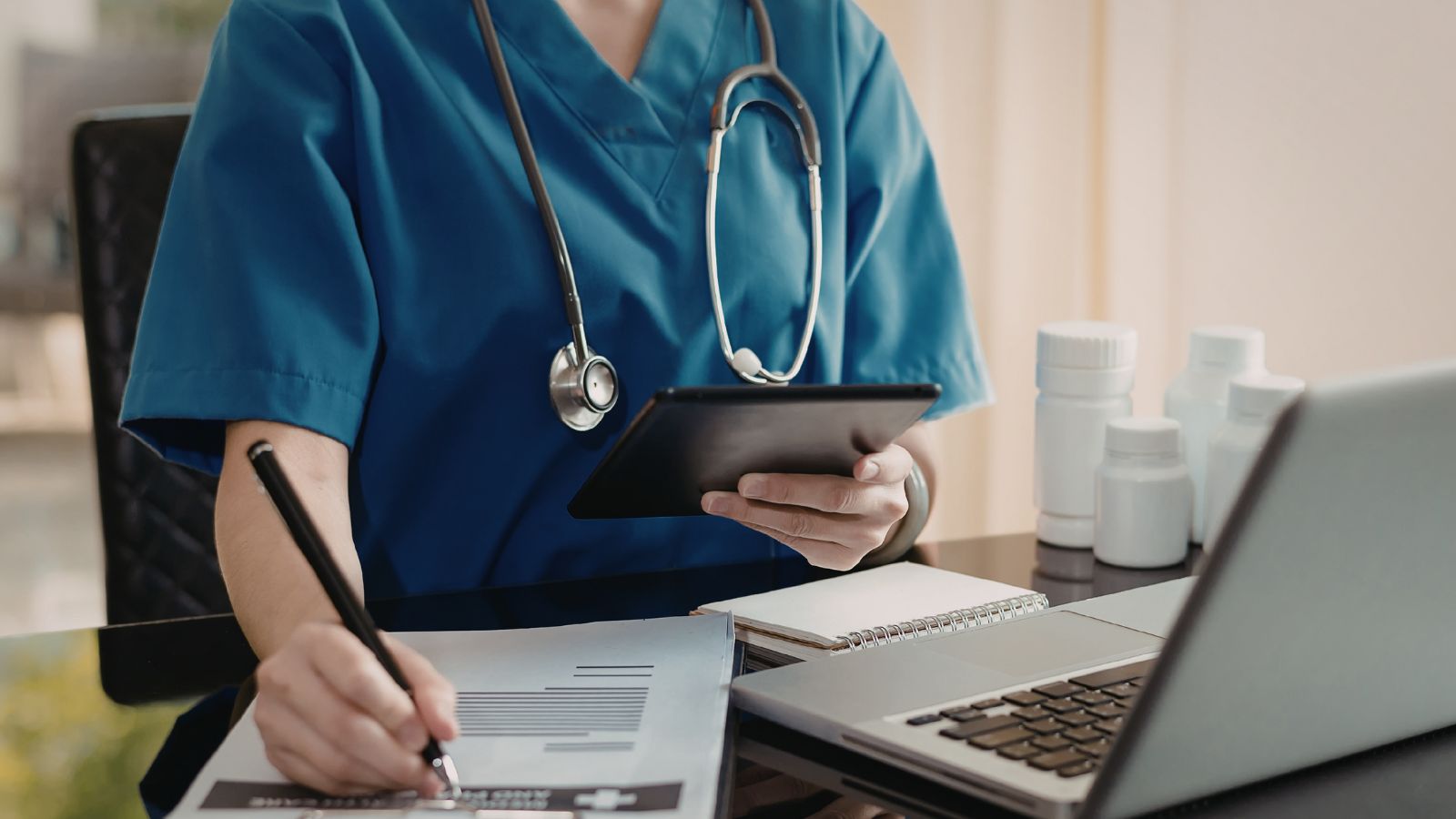 A nurse working at a desk on the computer with many papaers