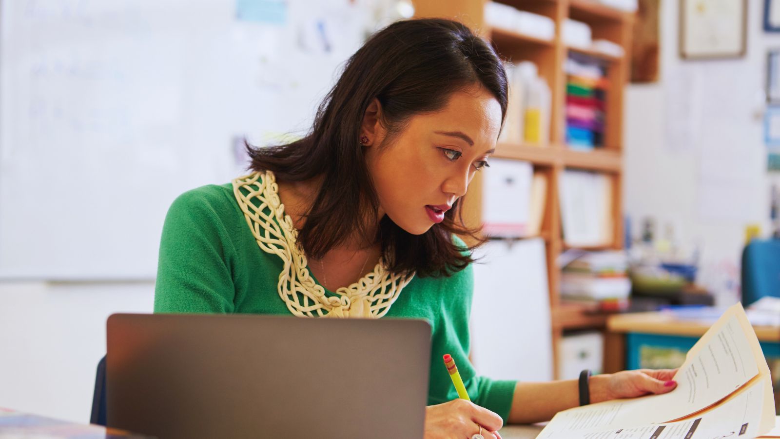 A teacher at a classroom desk grading papers.