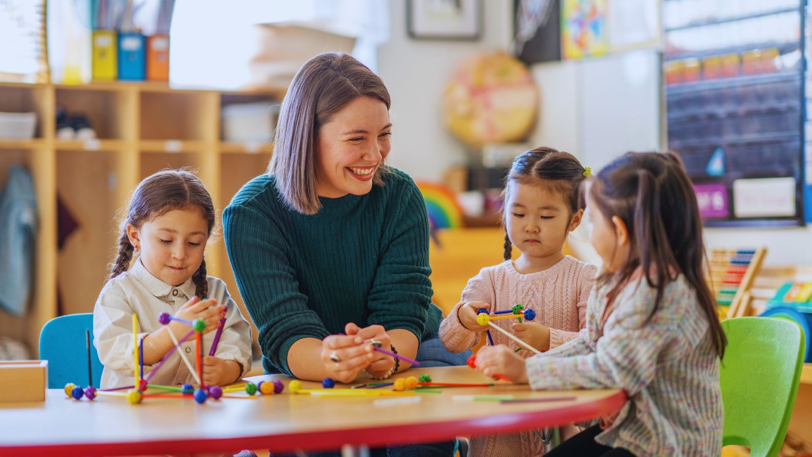 A smiling teacher sitting at a table with three young students.