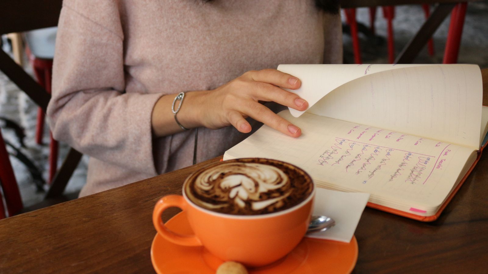 A hand flipping through previous pages of a wellness journal, with handwritten entries visible across multiple days.